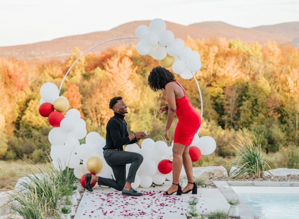 Man proposing on one knee inside a balloon arch setup at a private Airbnb in Sutton, Eastern Townships, with stunning fall foliage in the background