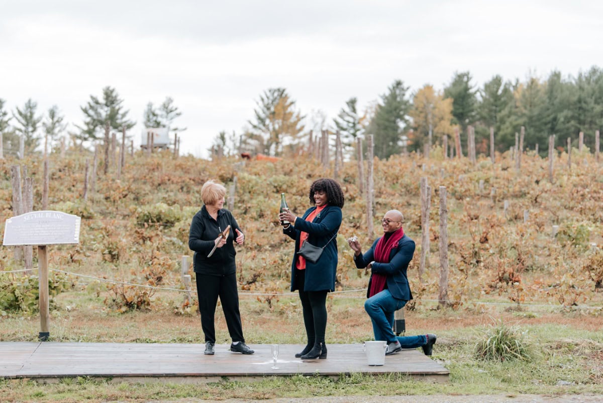 Man proposing on one knee during a champagne sabering experience at Le Cep d'Argent vineyard in Magog, Eastern Townships