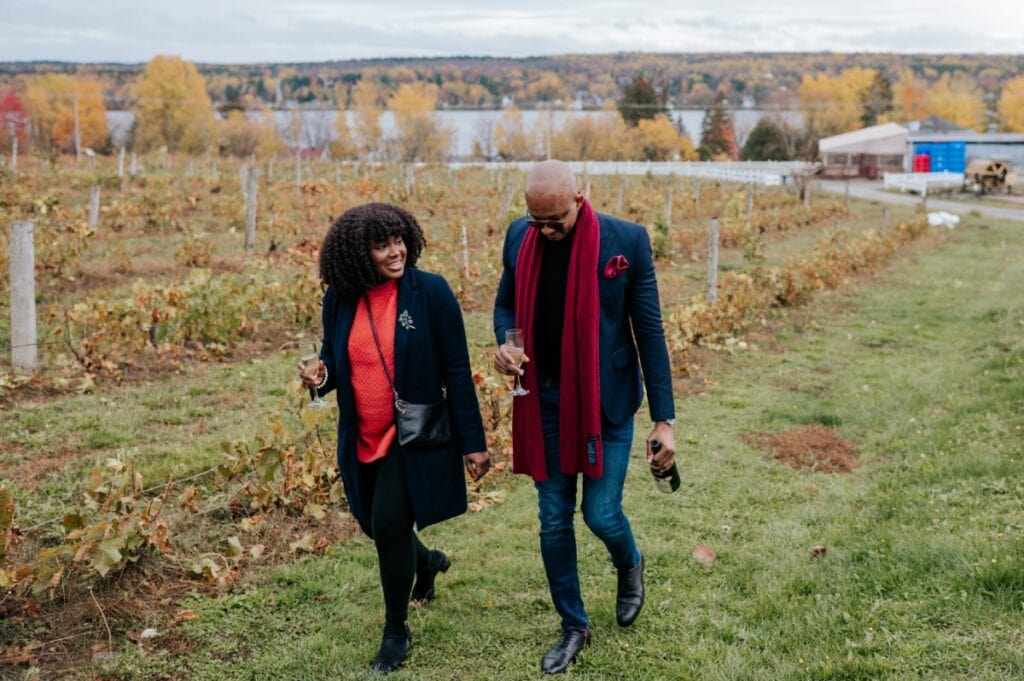 Newly engaged couple walking through the vineyards with champagne at Le Cep d'Argent in Magog, Eastern Townships proposal photography