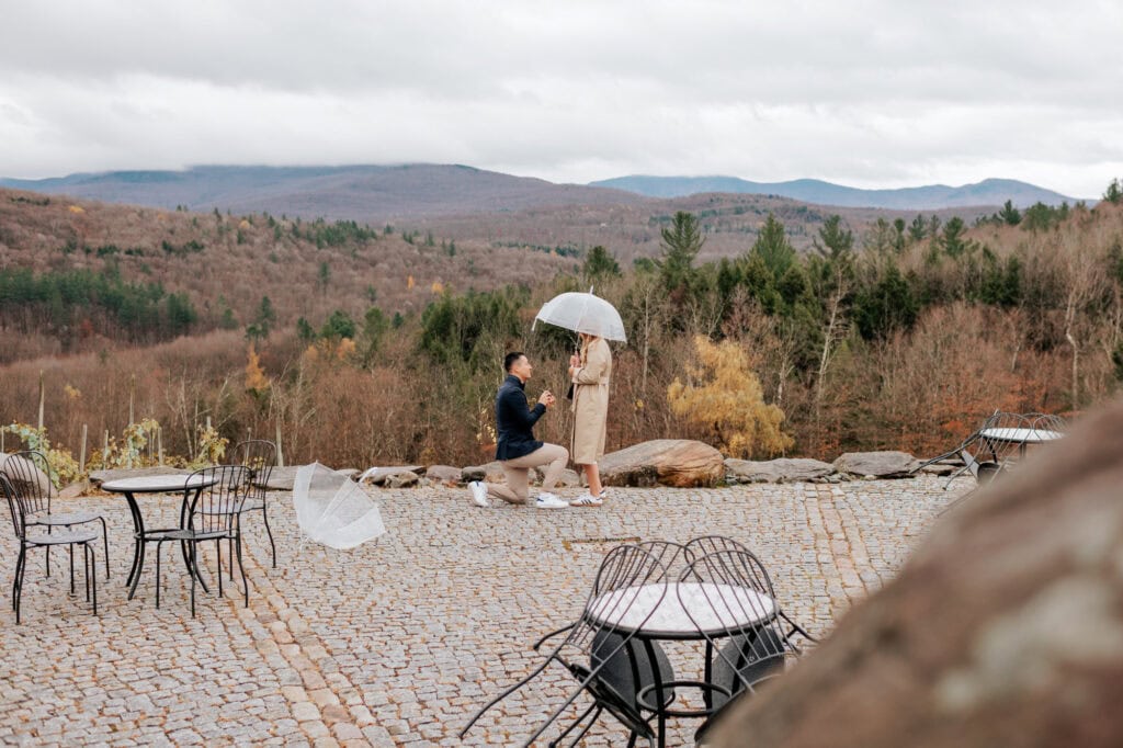 Man proposing on one knee on the terrace at Château Sainte-Agnès in Sutton, with the Eastern Townships mountains in the background